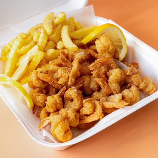 A white takeout container filled with golden-brown fried shrimp, crinkle-cut fries, and lemon wedges.