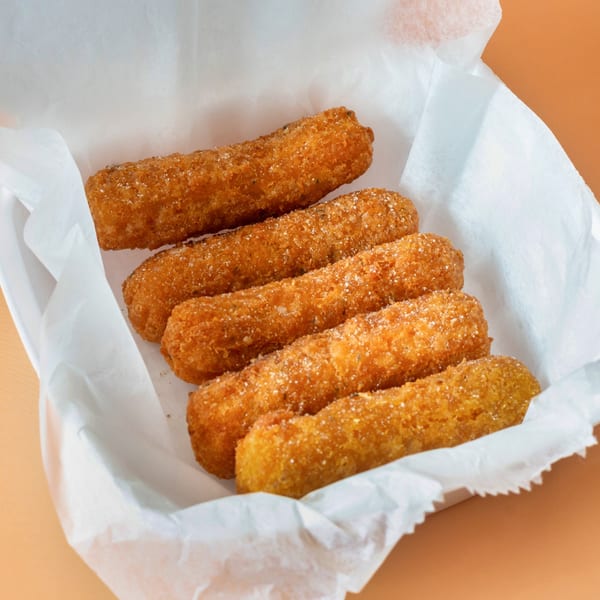 Five golden-brown fried mozzarella sticks, sprinkled with seasoning, in a white paper-lined basket.
