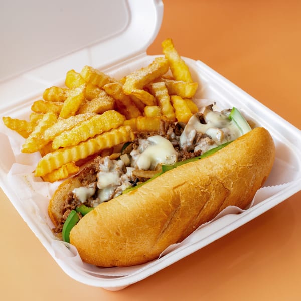Cheesesteak sandwich with melted cheese, green peppers, and onions, served with crinkle-cut fries.